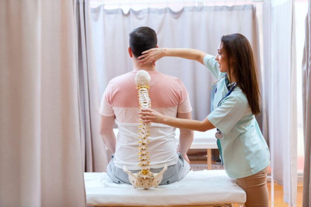 Chiropractor assessing a patient’s spinal alignment using a spine model as a guide