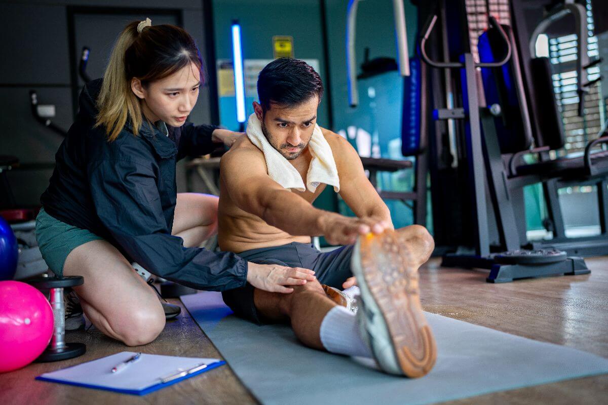 Trainer guiding an athlete through stretching exercises on a gym mat